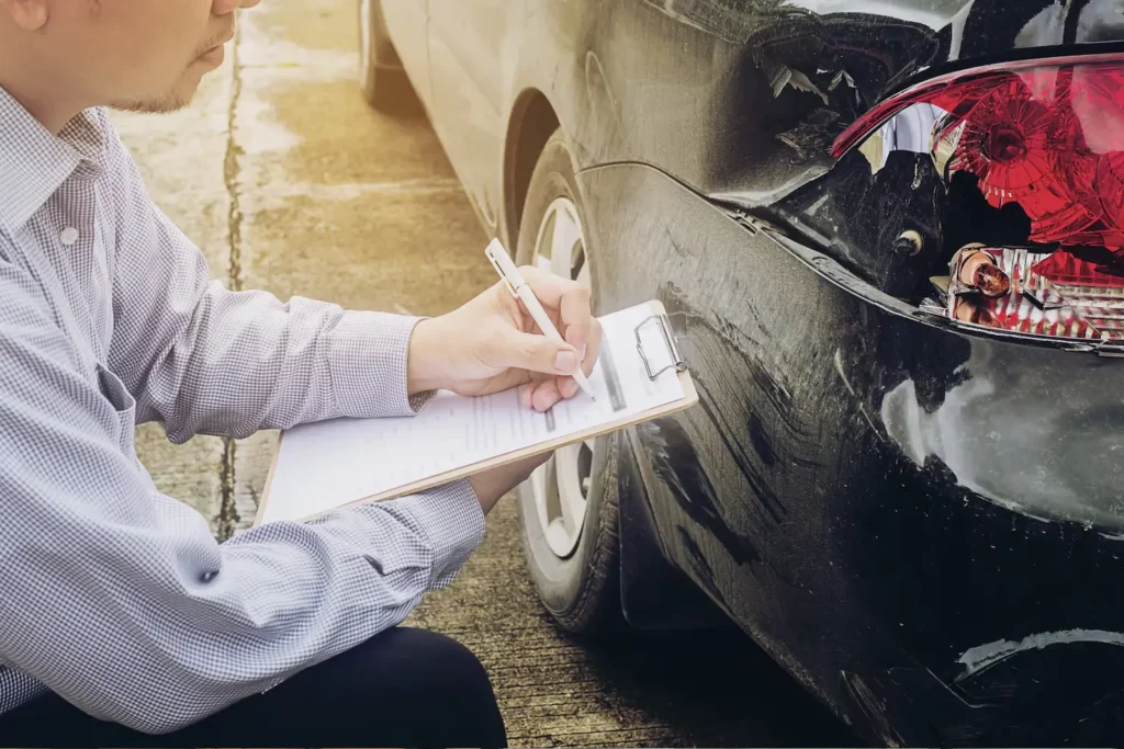 Man documenting damage on a black car after an accident, emphasizing vehicle repair and insurance claims in Grayson County personal injury context.