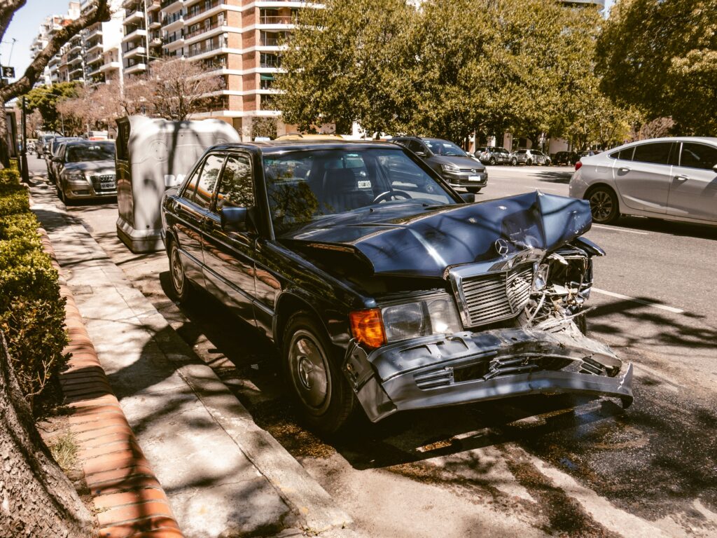 Damaged black car with front-end collision, parked on urban street, surrounded by trees and buildings, illustrating accident aftermath relevant to personal injury claims in Far North Dallas.