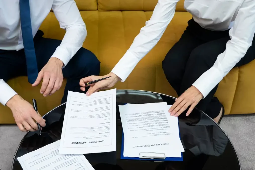 Two professionals reviewing and signing legal documents on a glass table, emphasizing legal consultation services for accident victims in Hot Wells.