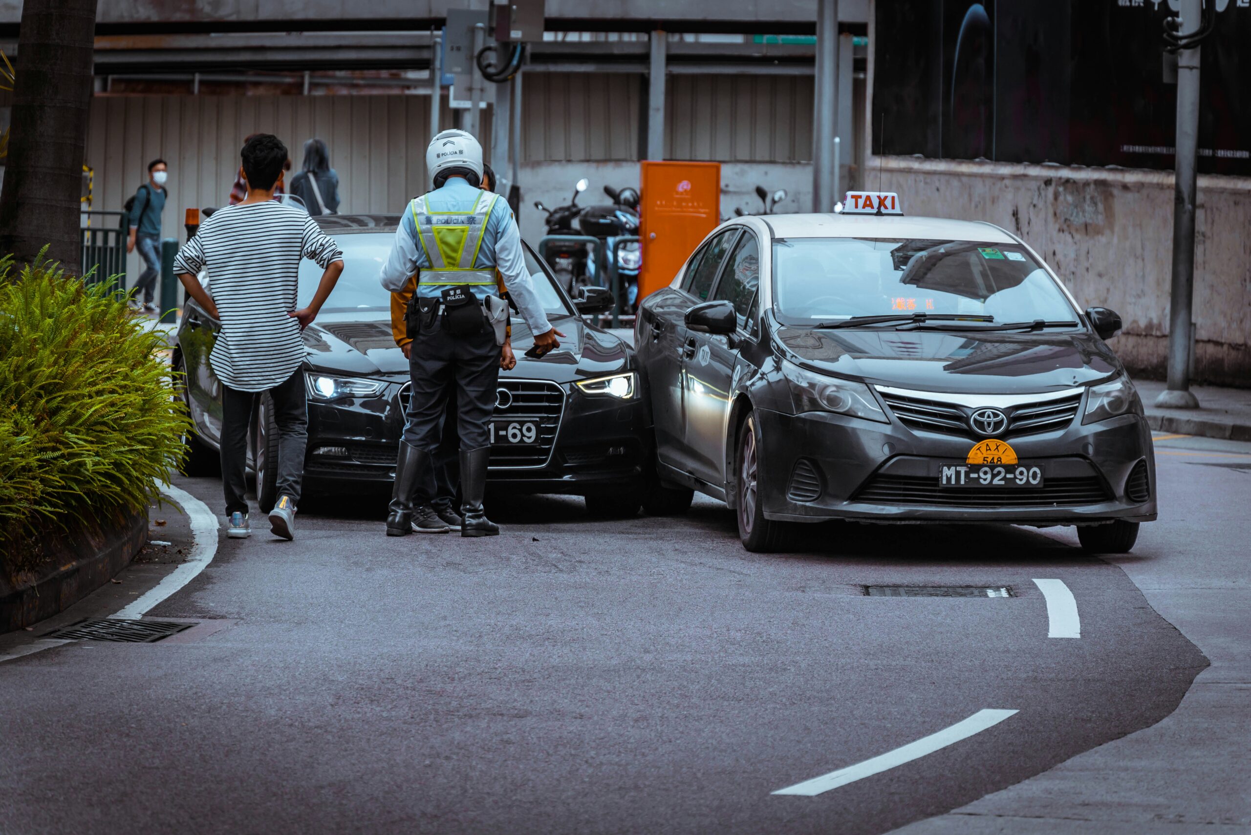 Car accident scene with a police officer assisting two drivers, one in a black car and the other in a taxi, in Midtown Houston, emphasizing legal support for accident victims.