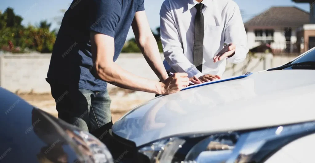 Two men discussing auto accident details, one writing on a clipboard on a car hood, representing legal consultations for car accident claims in Greater Harmony Hills.
